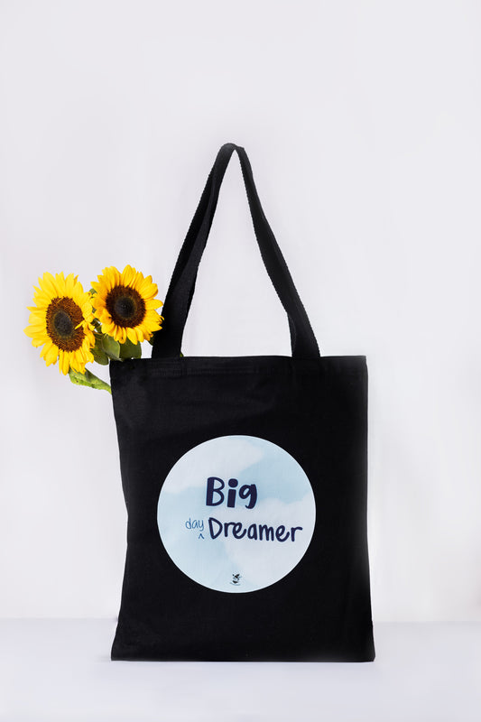 A black tote bag with a cloud-blue circular print that reads 'Big Dreamer'.