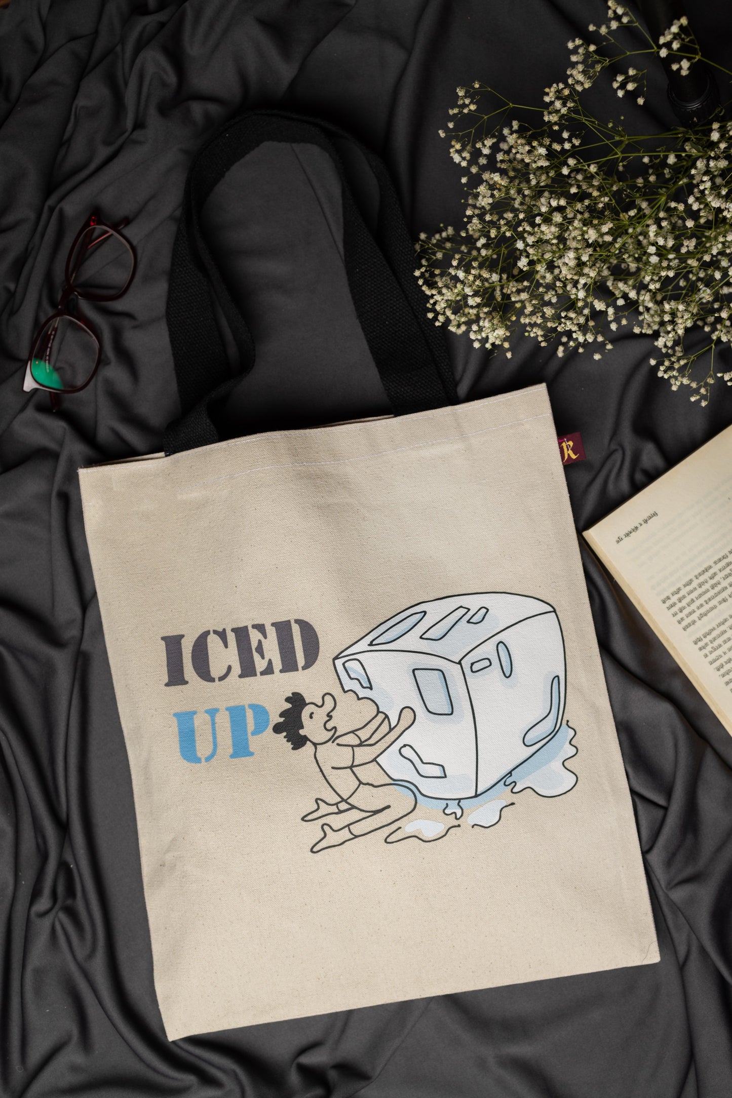 Beige tote bag with 'ICED UP' graphic design on a black fabric background