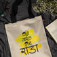 Beige tote bag with yellow and black text on a dark fabric background with flowers and glasses.