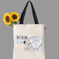 A off white cotton tote bag with 'ICED UP' printed on it, featuring a whimsical illustration of a character hugging a giant ice cube. The bag has black handles.