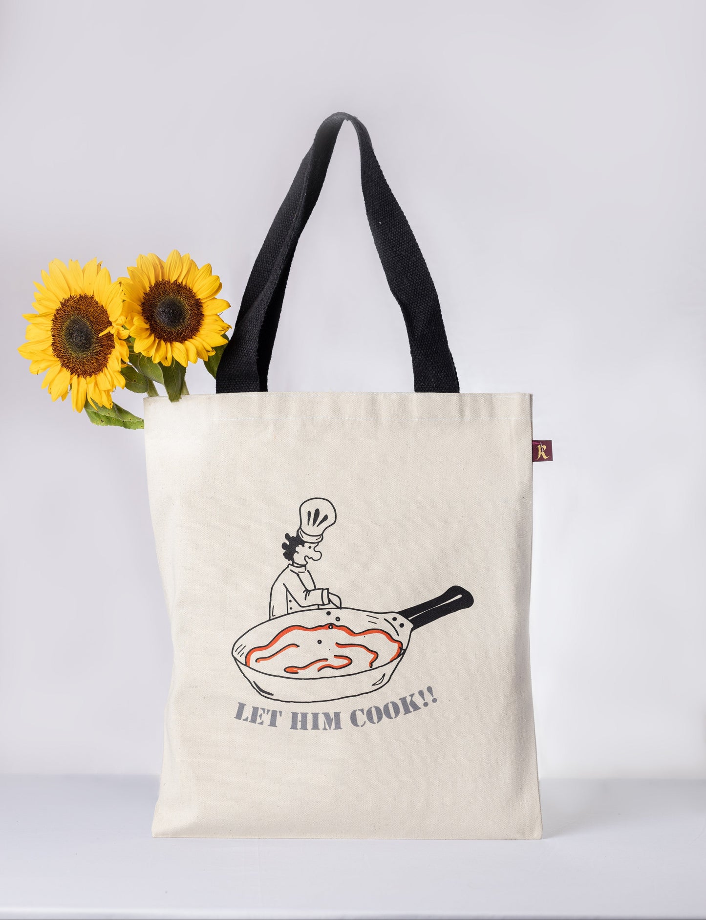 Tote bag with a graphic design of a person cooking in a pan and text 'LET HIM COOK!' 
