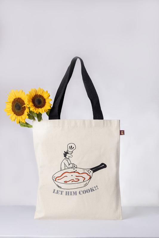 Tote bag with a graphic design of a person cooking in a pan and text 'LET HIM COOK!' 