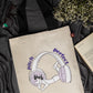 Beige tote bag with headphone illustration and text on a dark fabric background