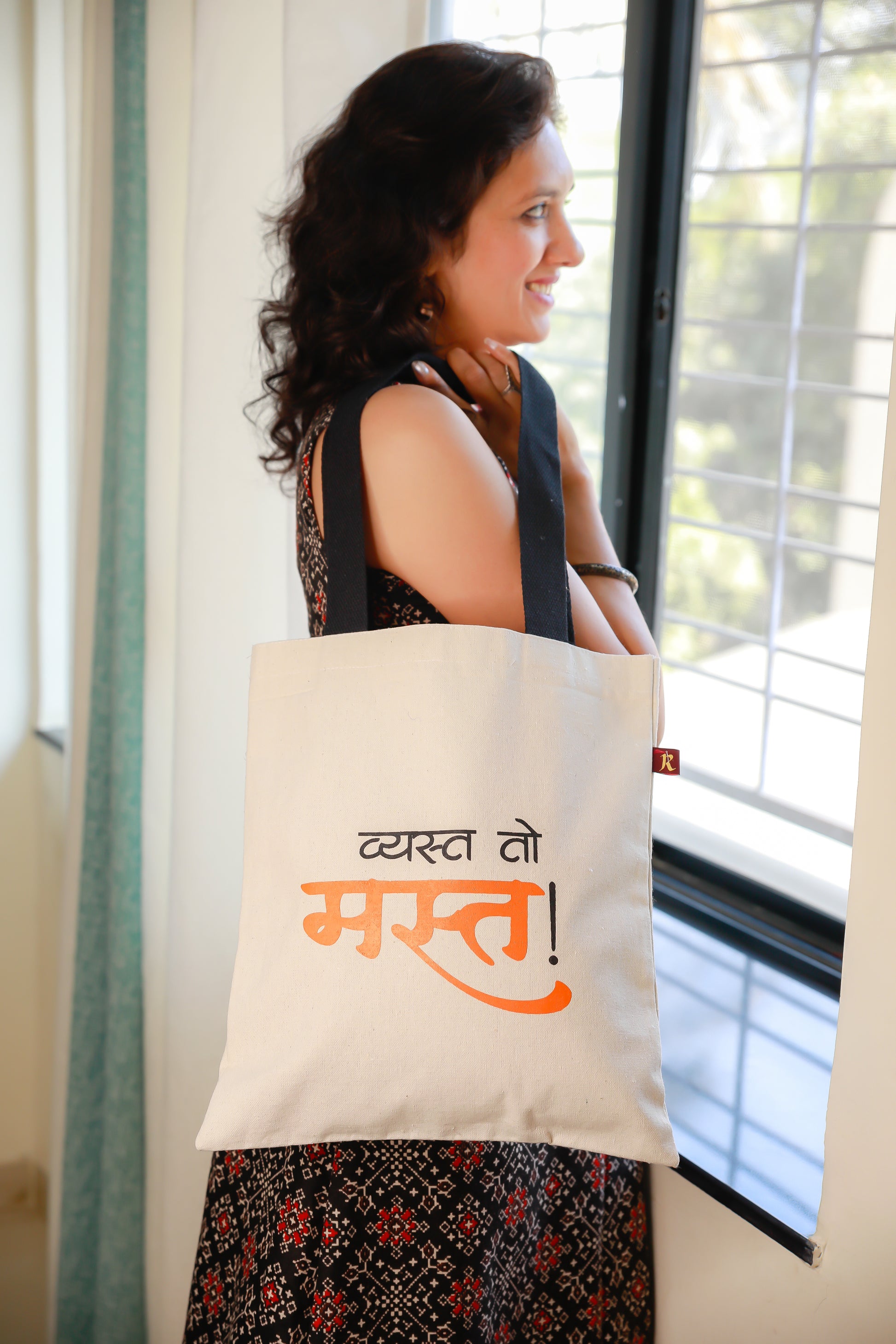 A person holding a beige flat tote bag with black straps and text printed in Marathi