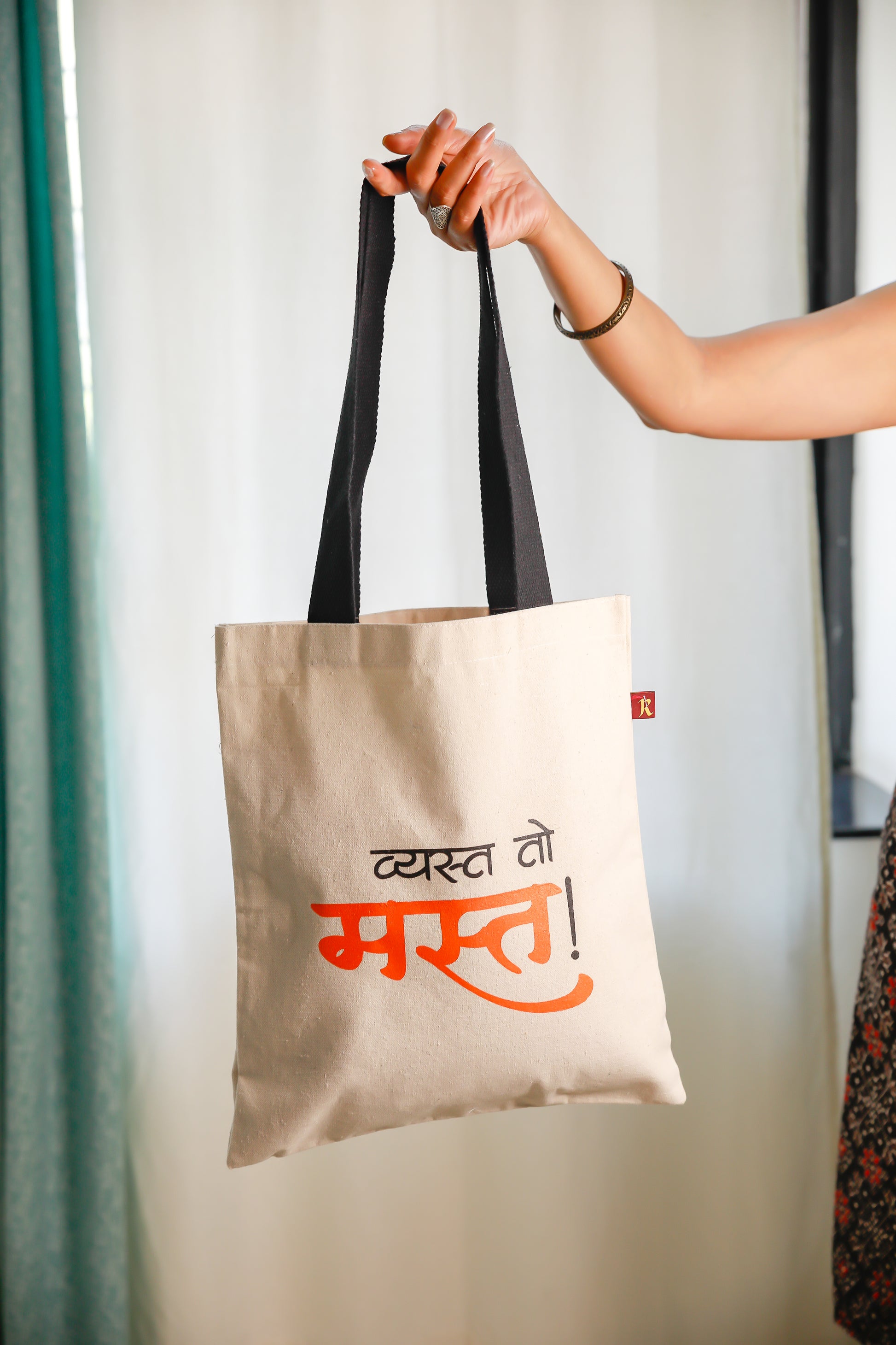 A person holding a beige flat tote bag with black straps and text printed in Marathi